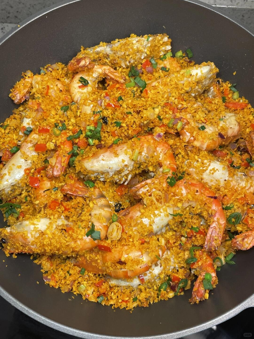 Whole prawns covered in golden crumbs with red peppers and green herbs on a pale plate.