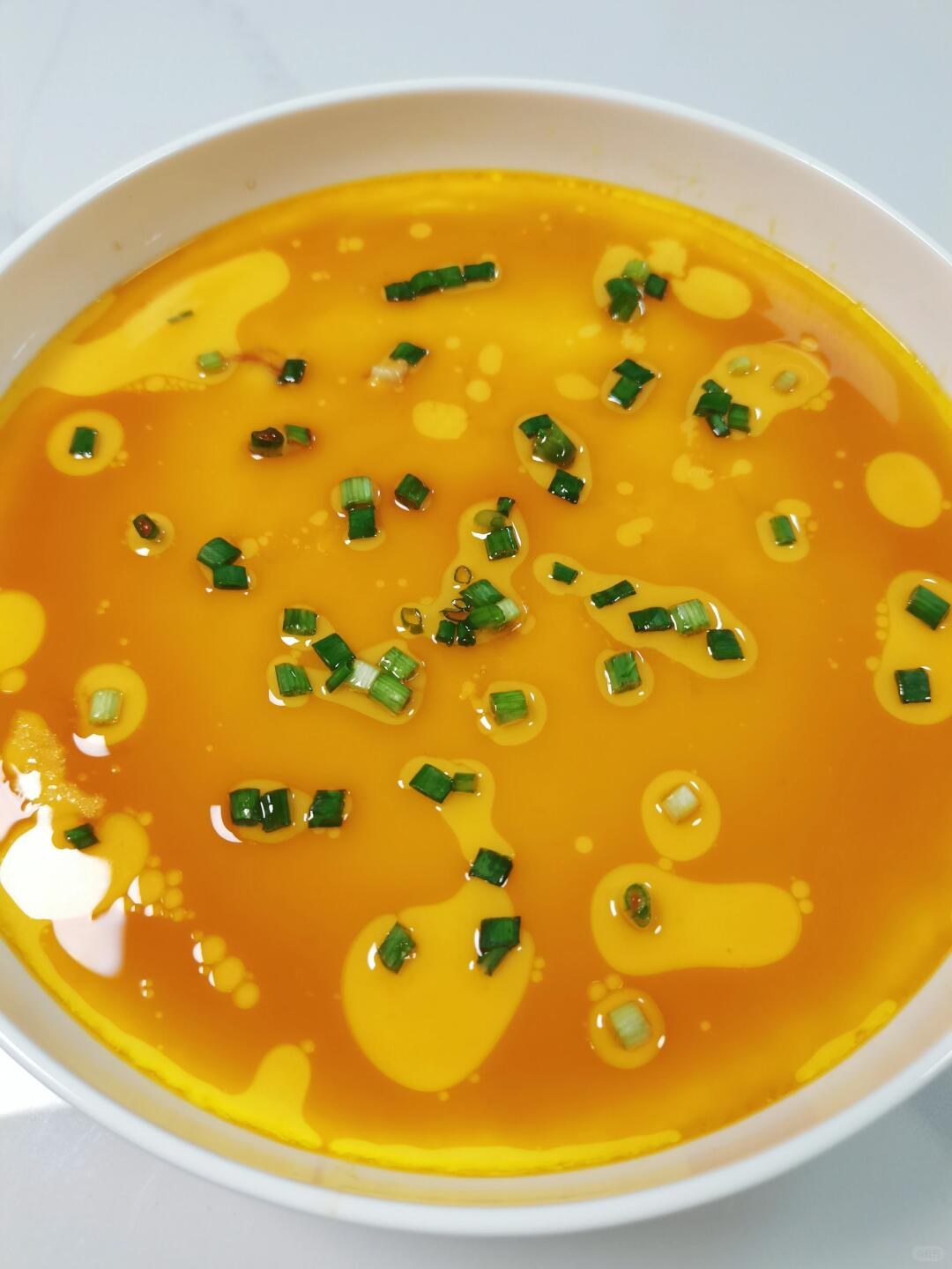 Smooth yellow steamed egg custard topped with chopped scallions and oil in a white bowl.