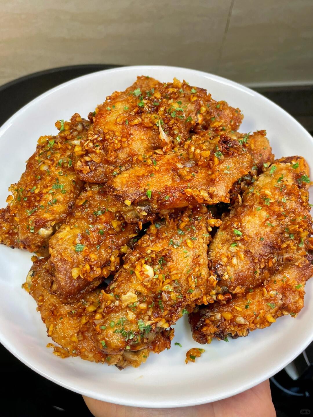 Golden chicken wings coated with minced garlic and green herb flecks on a white plate.