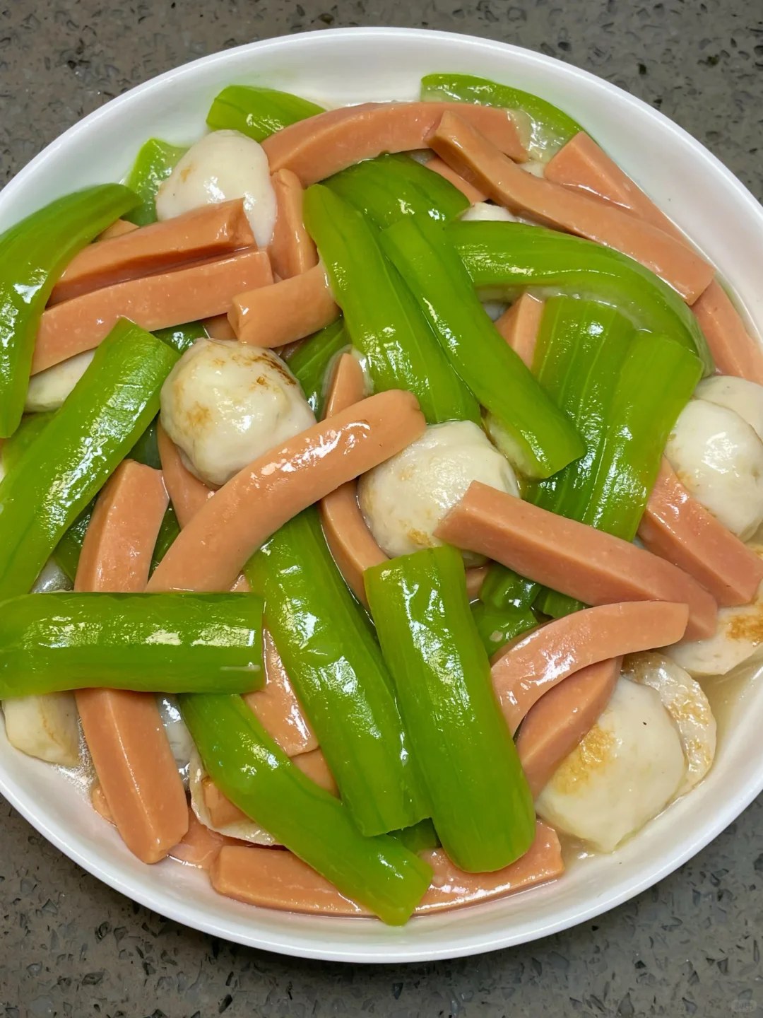 Green luffa pieces, pale seafood balls and strips of pink sausage on a white plate.