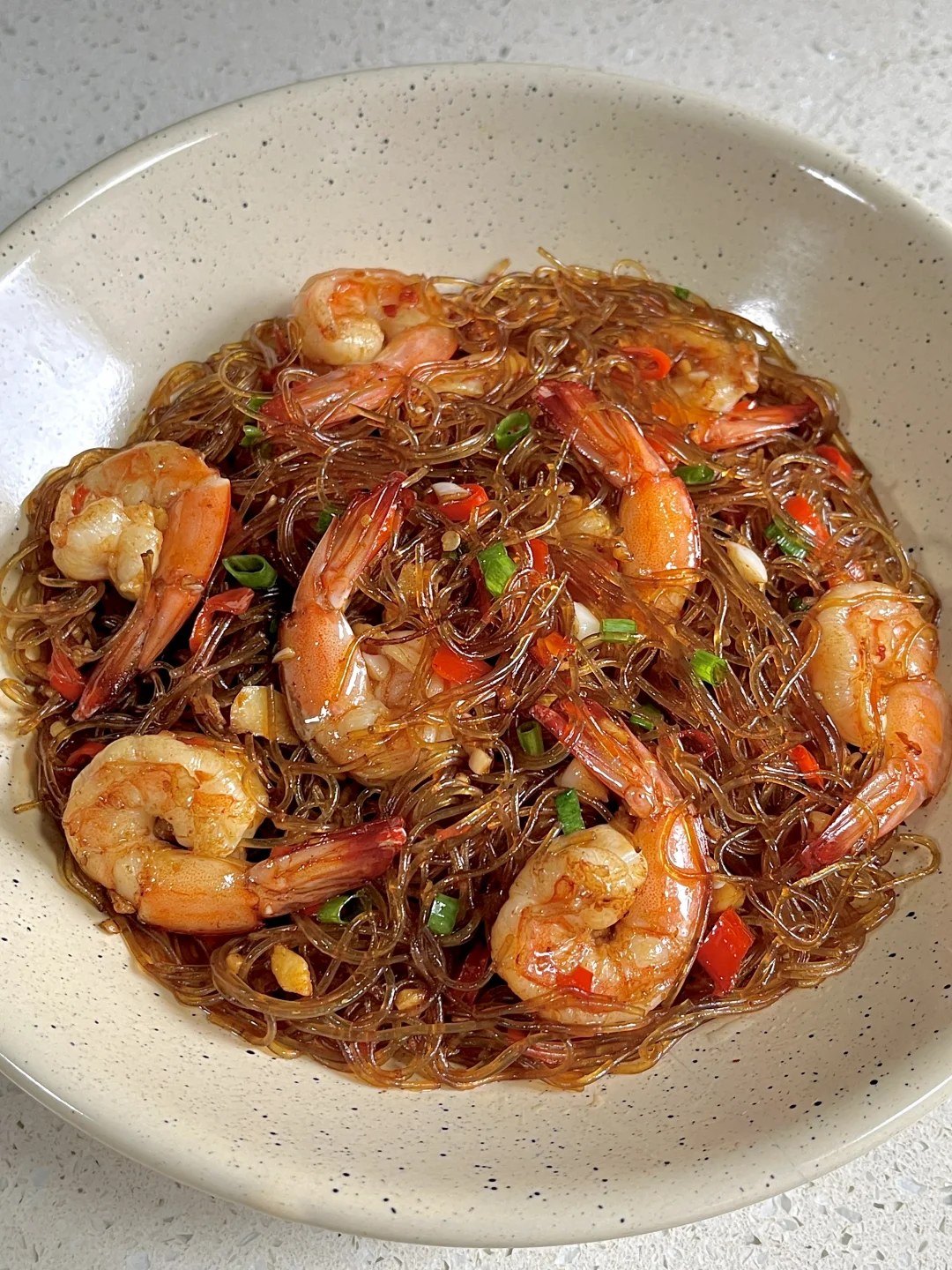 Shrimp and brown glass noodles with chopped chiles and scallions in a pale bowl.