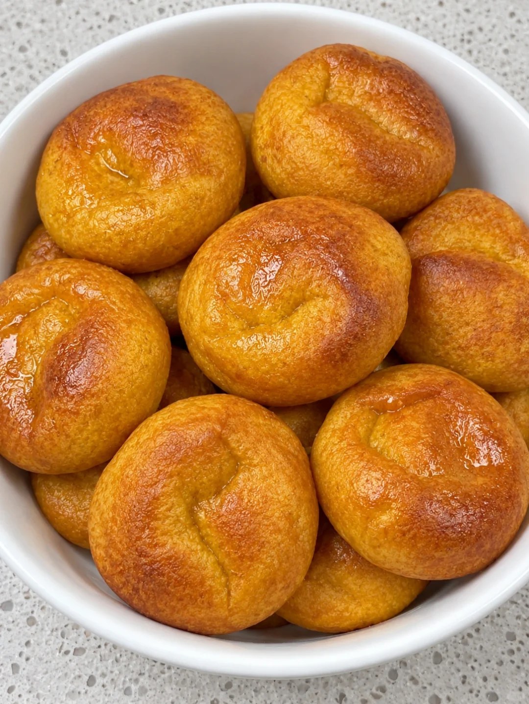 Small round golden pumpkin cakes in a white bowl.
