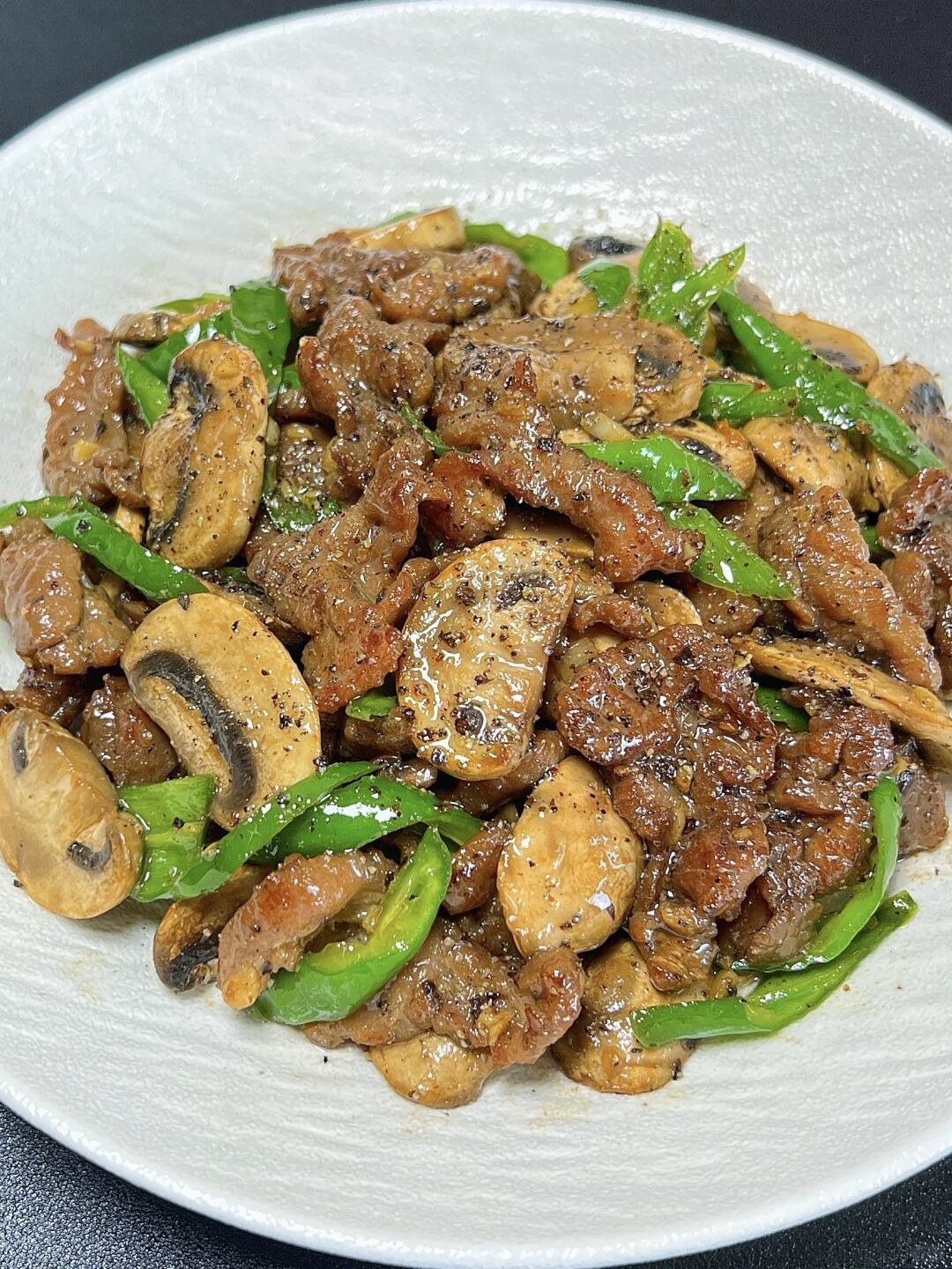 Sliced beef and button mushrooms with green pepper pieces on a pale plate.